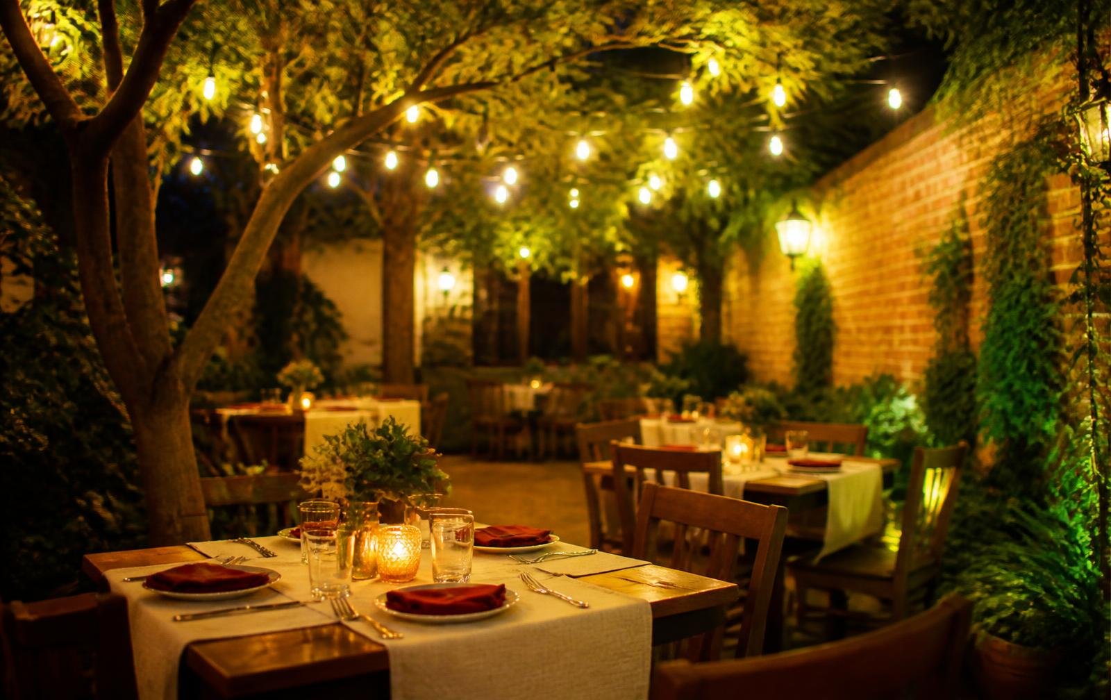 Cafe Scarlet's outdoor courtyard at night, string lights over tables surrounded by greenery